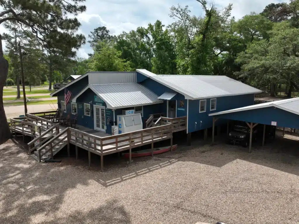 Aerial view of a blue RV park office building with wooden deck, ice machine, American flag, and covered parking area.